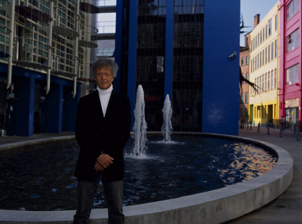 Man in front of Fountain and colourful building