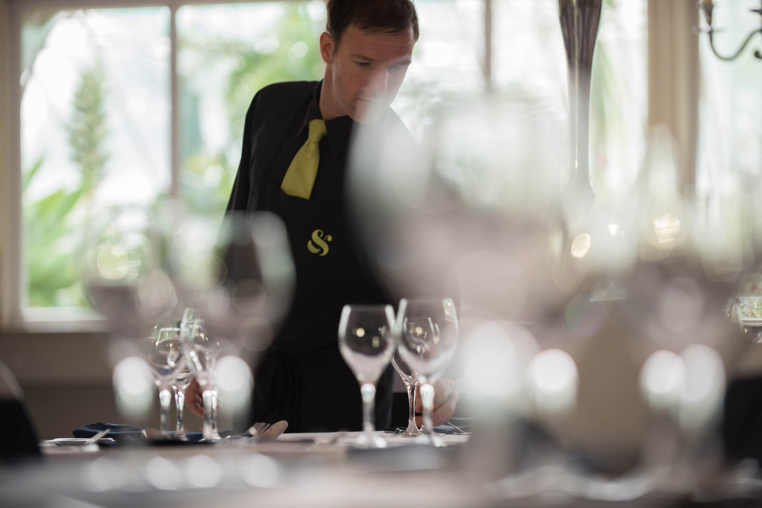 man laying table in soft focus with glasses in foreground.