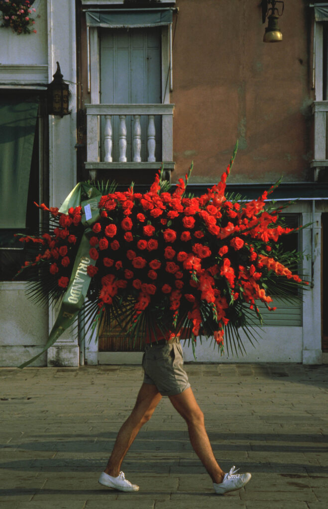 man beneath bunch of flowers- walking along Venice Grand Canal