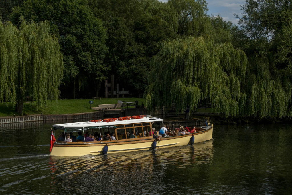 cruise boat with passengers on river with willows behind