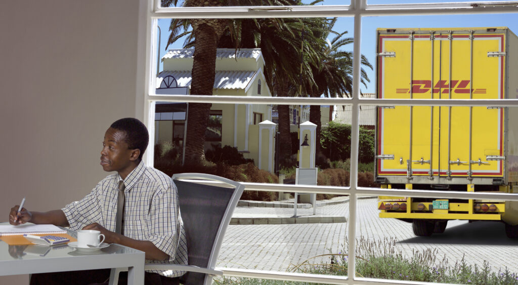 Man in office with DHL truck in background on service road