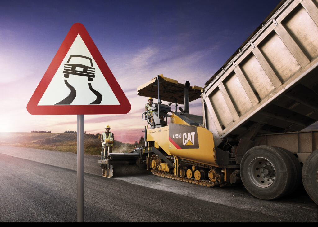 road with caterpillar road making equipment and road sign showing car and squiggle