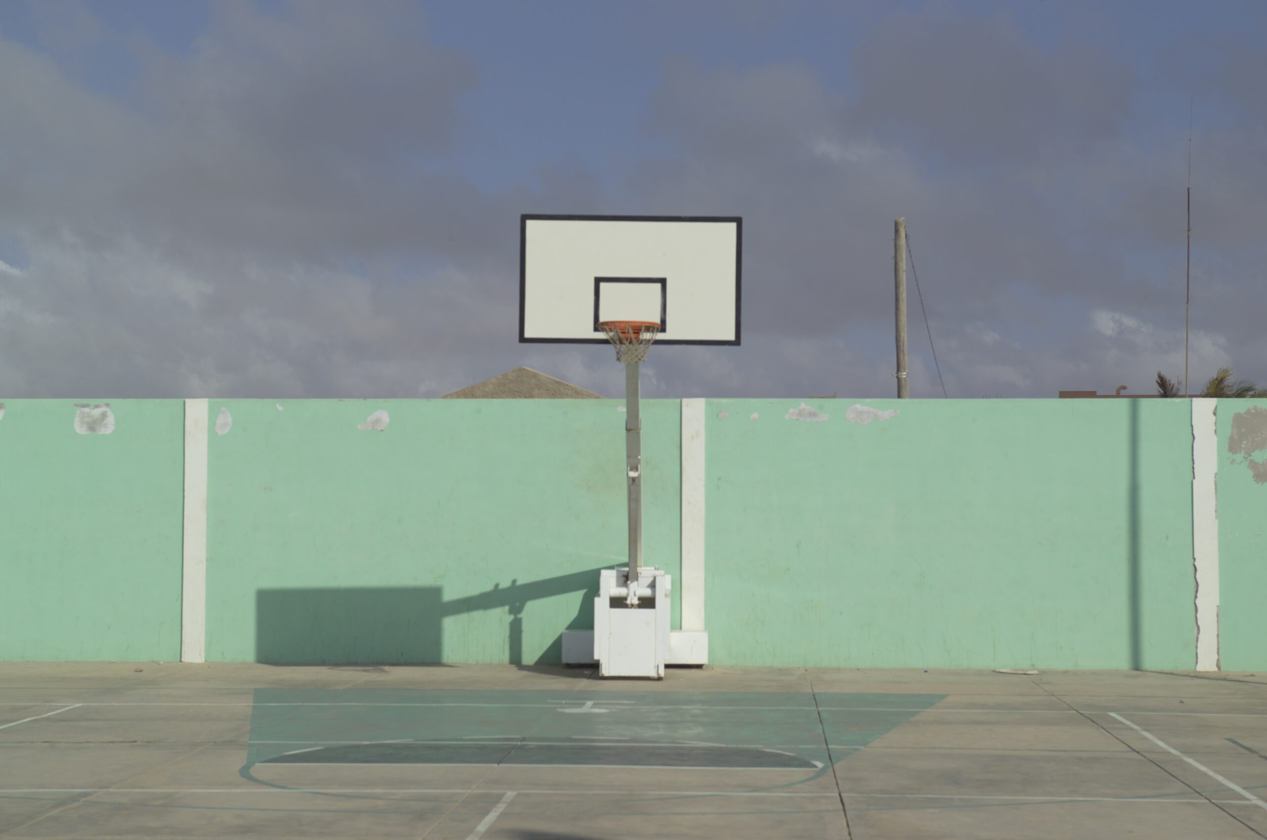 Green wall with foreground of a Basketball hoop, in afternoon sun.