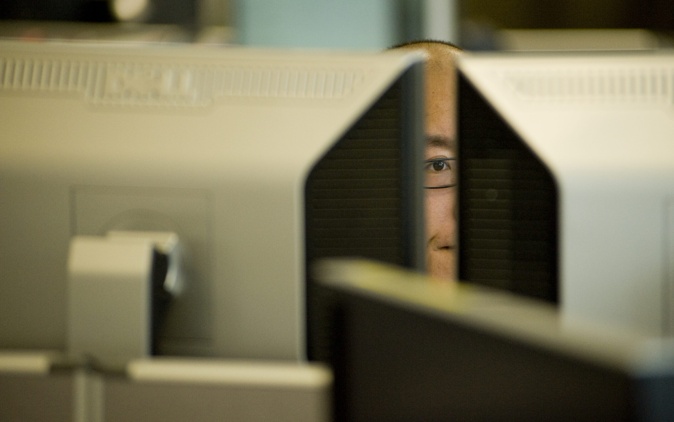 man's eye seen between back of computer screens seen from behind