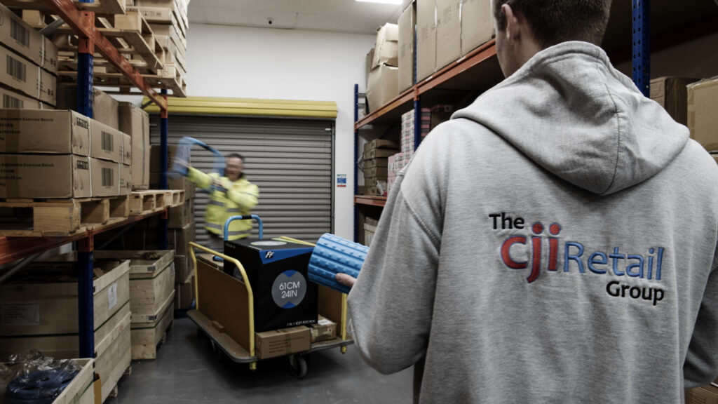 Man in Branded hoodie in warehouse man in background moving products onto trolley