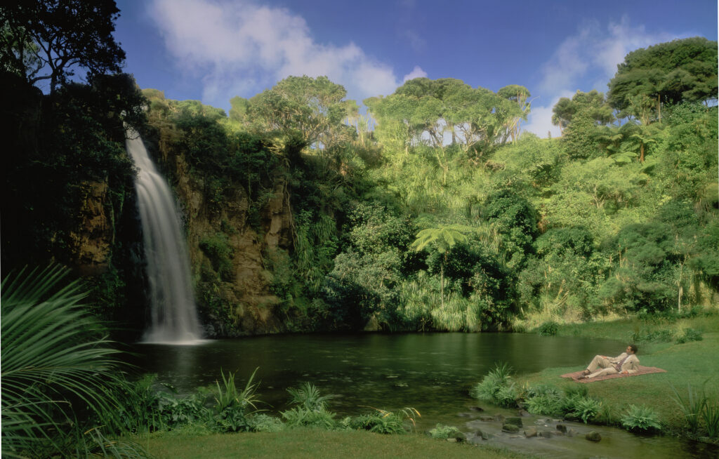tropical landscape with waterfall small pond and man lieing down in light suit