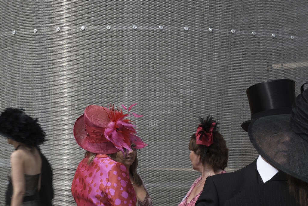 Ladies in fancy hats with no faces showing, man hidden apart from his Top hat against metallic background