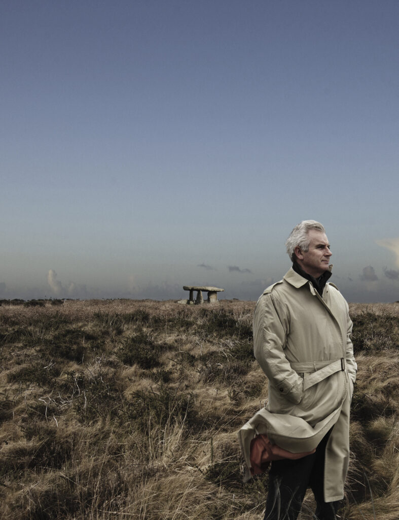 windswept man in landscape with ancient monument in background