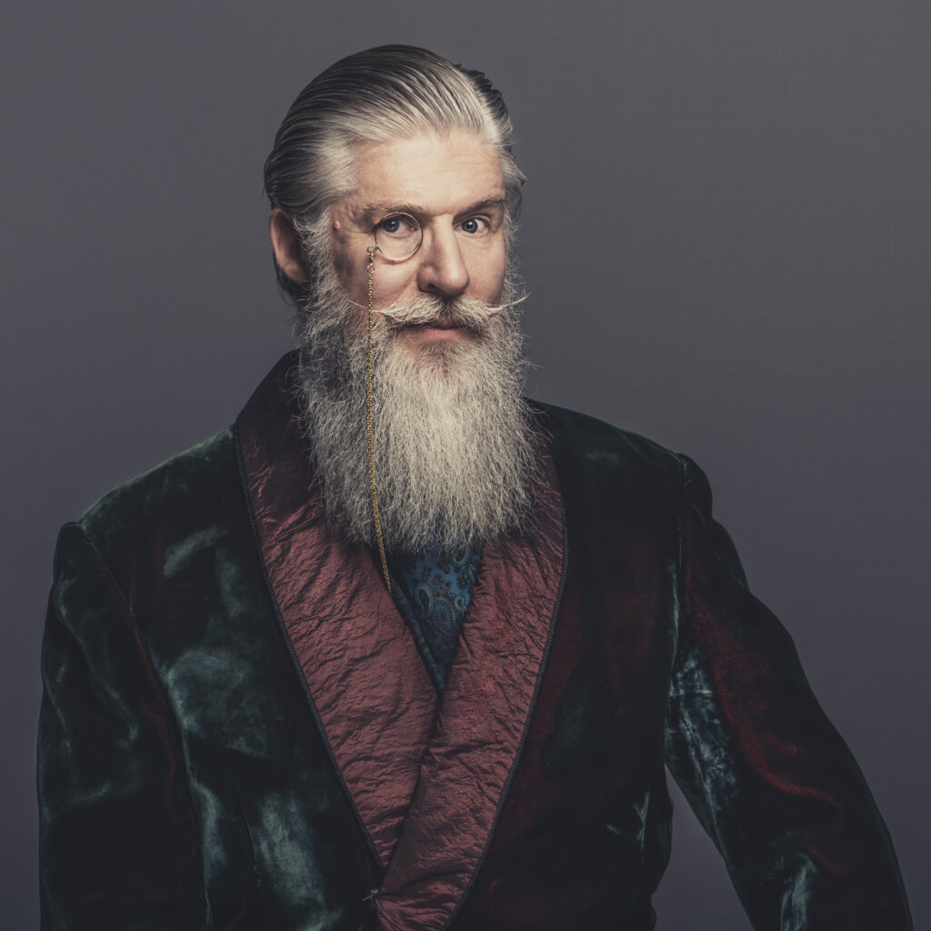 A bearded, distinguished gentlemen in a smoking jacket and wearing a monocle. Photograph for the Marsh & Parsons brand campaign by Gullachsen
