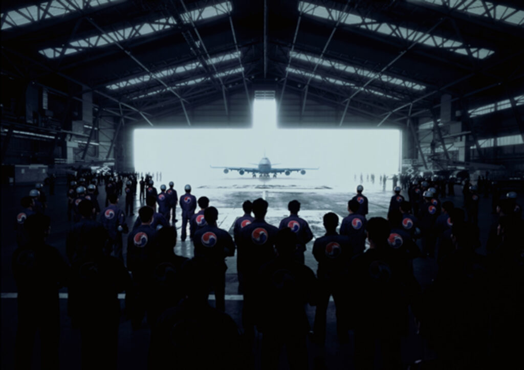 Aircraft entering Hanger with technicians in foreground awaiting the plane
