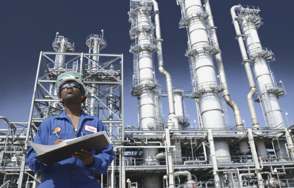 Man in uniform with Shell logo in front of chemical plant