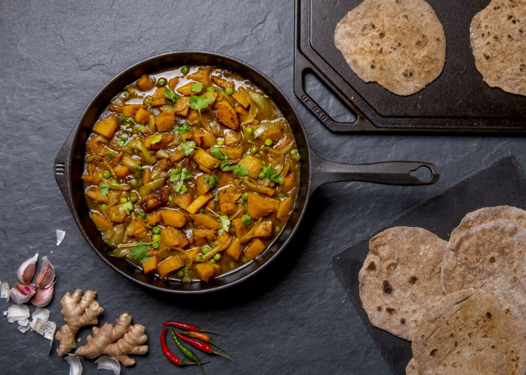 Iron Skillet from above, with butternut curry - plus flatbreads on cast iron flat griidle and raw ginger, garlic, chilli's on slate surface