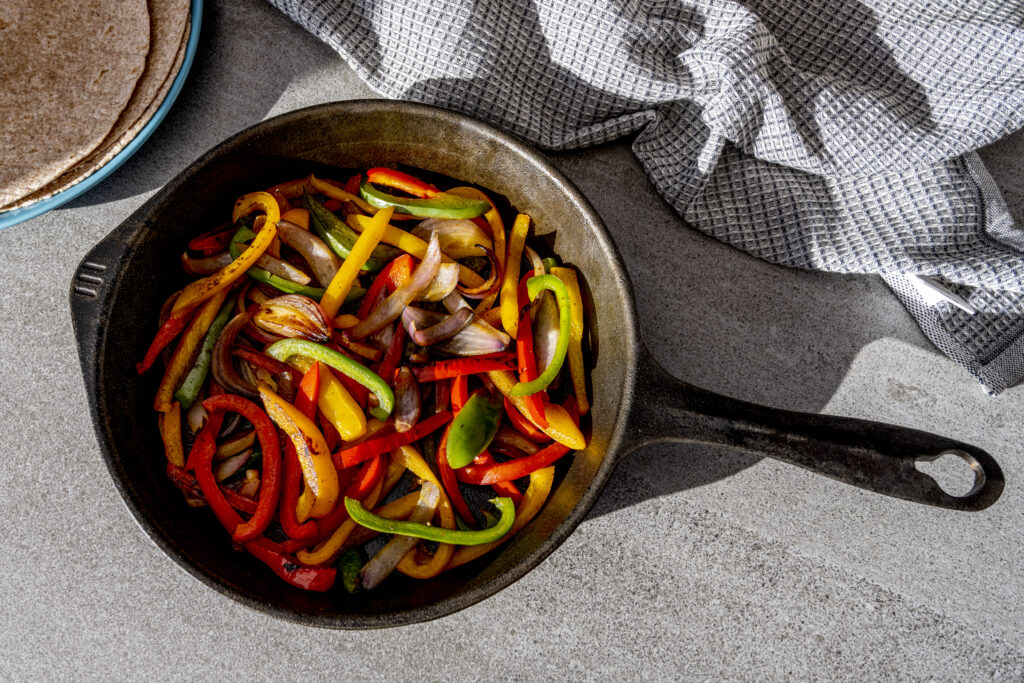 Cast iron skillet with peppers cooked - shadows on tile surface and cloth