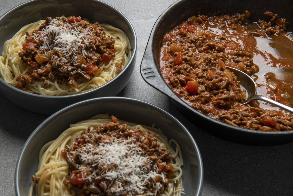 Spag Bog - Ragu of beef mince and tomatoes, in Cast iron skillet with bowls of finished Spaghetti Bolognese