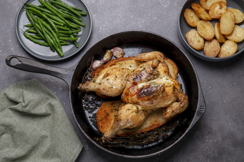 chicken in cast iron skillet on hard surface with green string beans on plate and saute potato