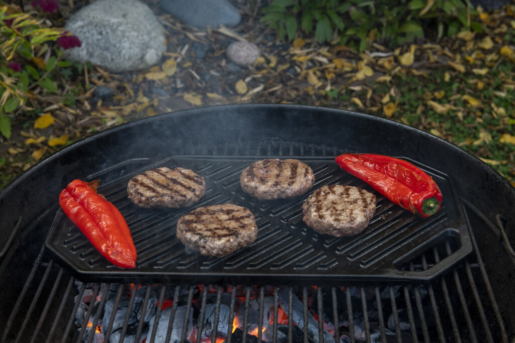 BBQ - Burgers and red peppers cooking over hot charcoal on Emba griddle