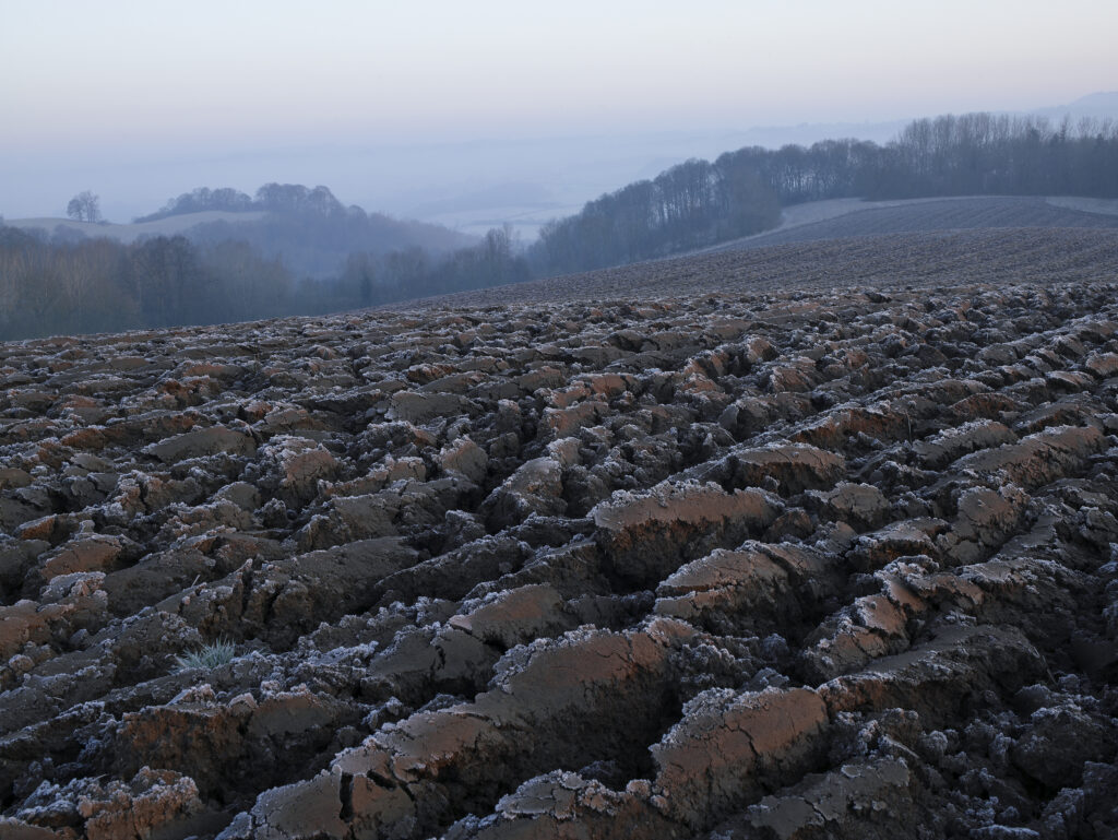 Ploughed field with frost on furrows with Vally in mist below