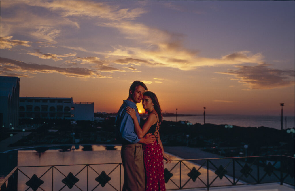 couple on rooftop overlooking pool with sun setting behind them