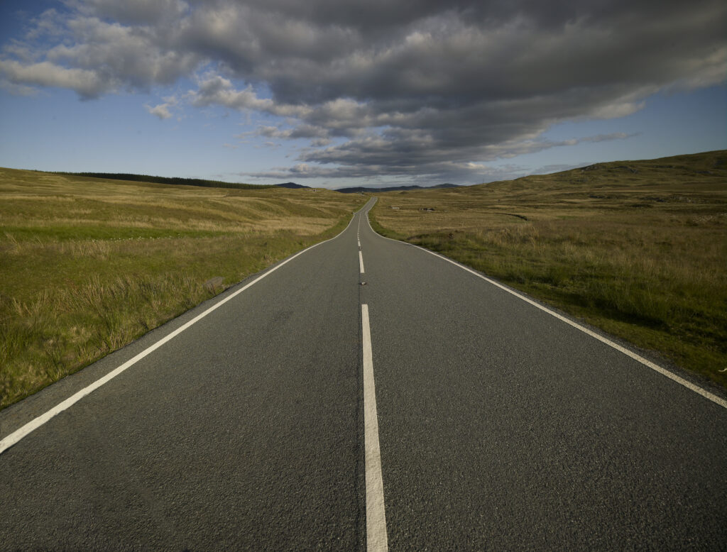 Road seen from centre going away to vanishing point, with big sky and clouds