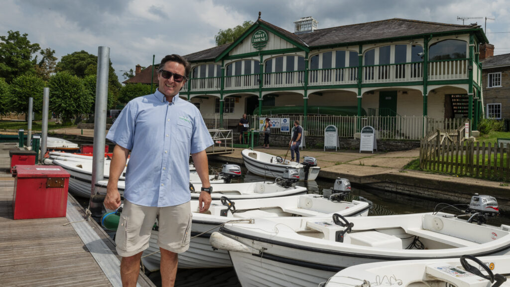 man with boats and boathouse behind -
