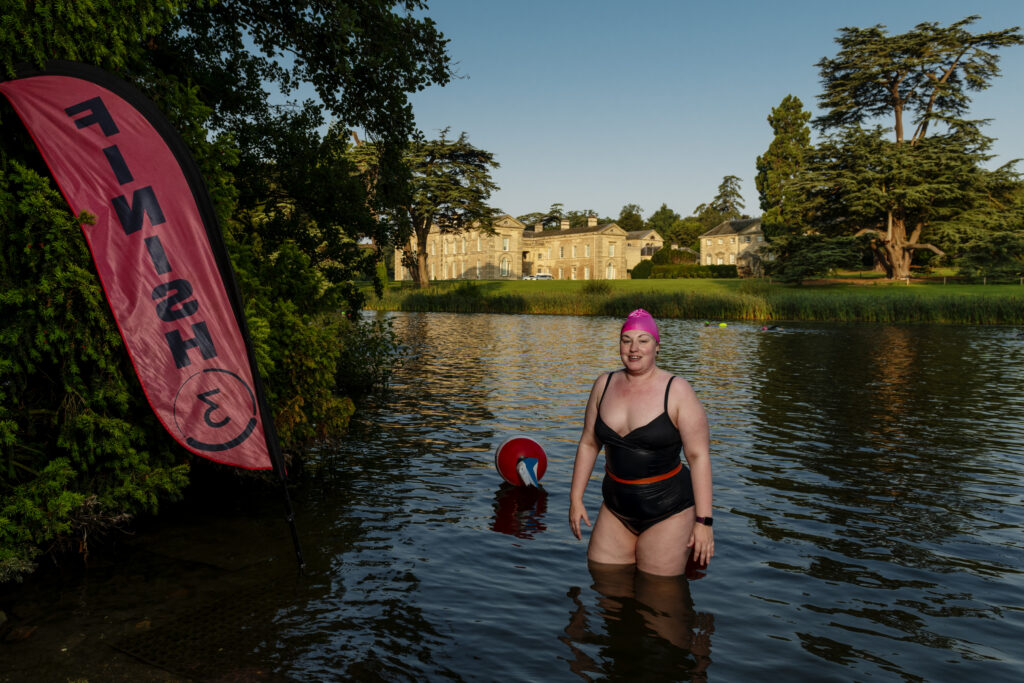lady in lake with swimming costume exiting at Finish with Stately Home , Compton Verney in BAckground