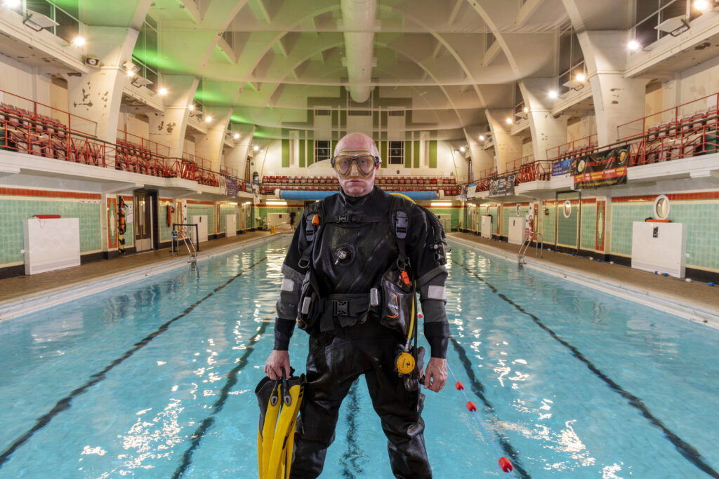Man with swimming pool behind, he in diving equiment and mask on