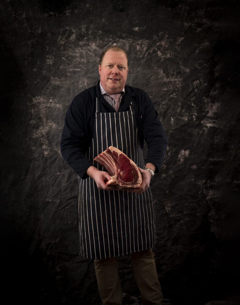 Business portrait photograph of a butcher holding a cut of meat. Taken for Smith & Binley Butchers.