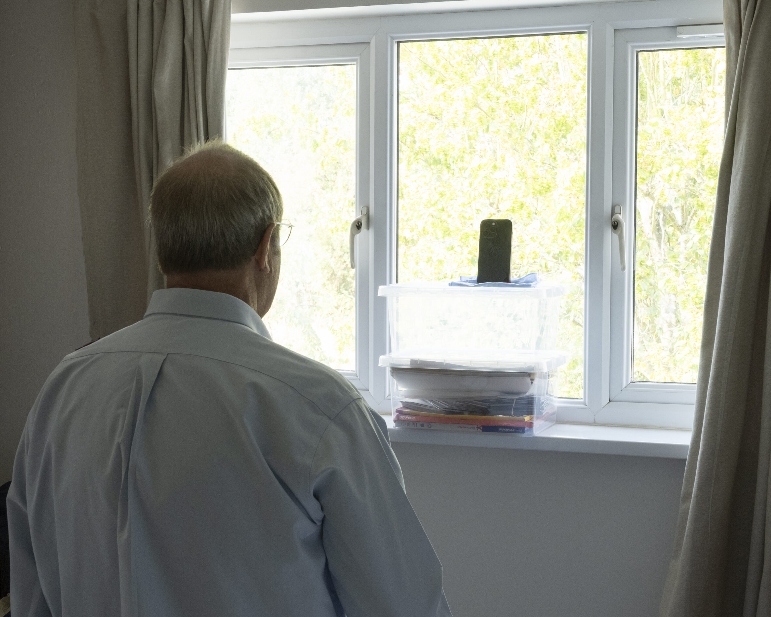 man looking at window with iphone propped on box